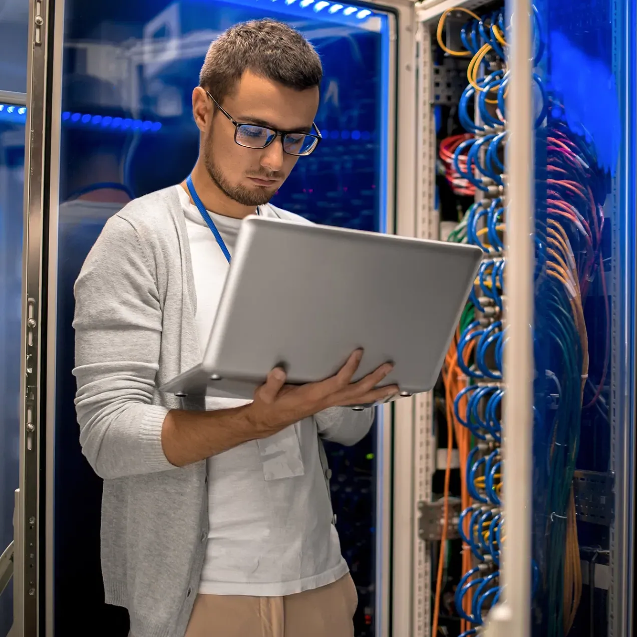 IT professional working on a laptop in a server room, managing network infrastructure and cybersecurity in the Information Technology program.